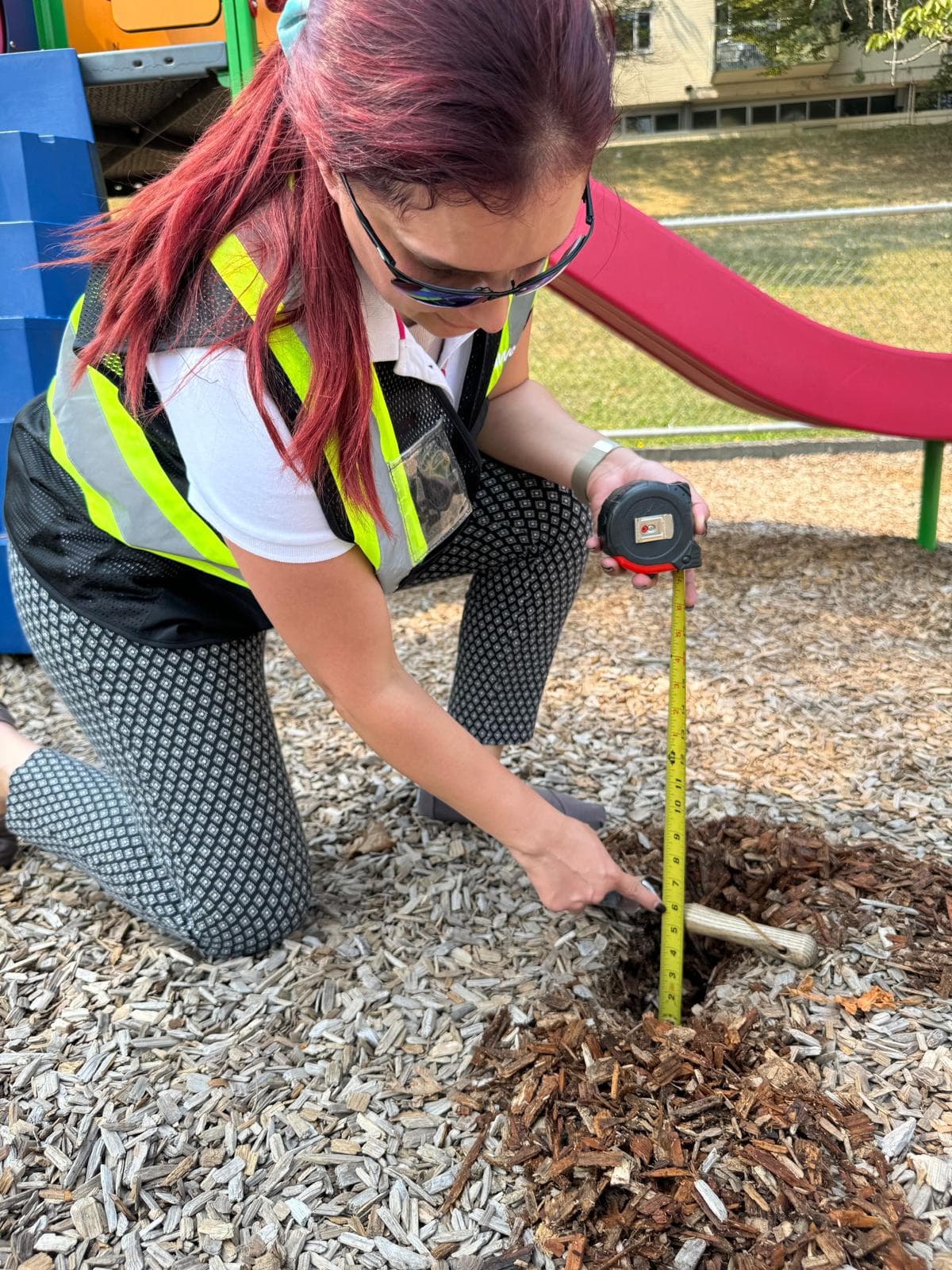Westplay inspector kneeling with a tape measure to check engineered wood fiber depth under a slide