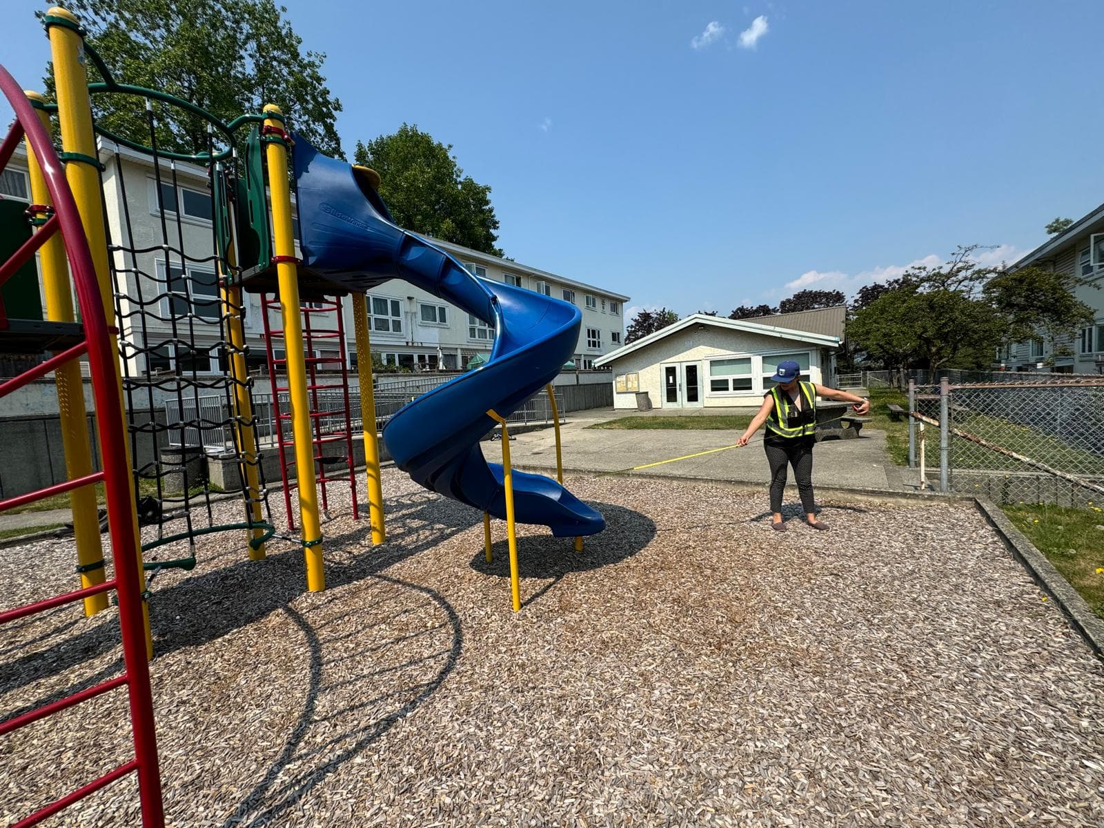 Westplay team member measuring the use zone around a blue spiral slide at a school playground