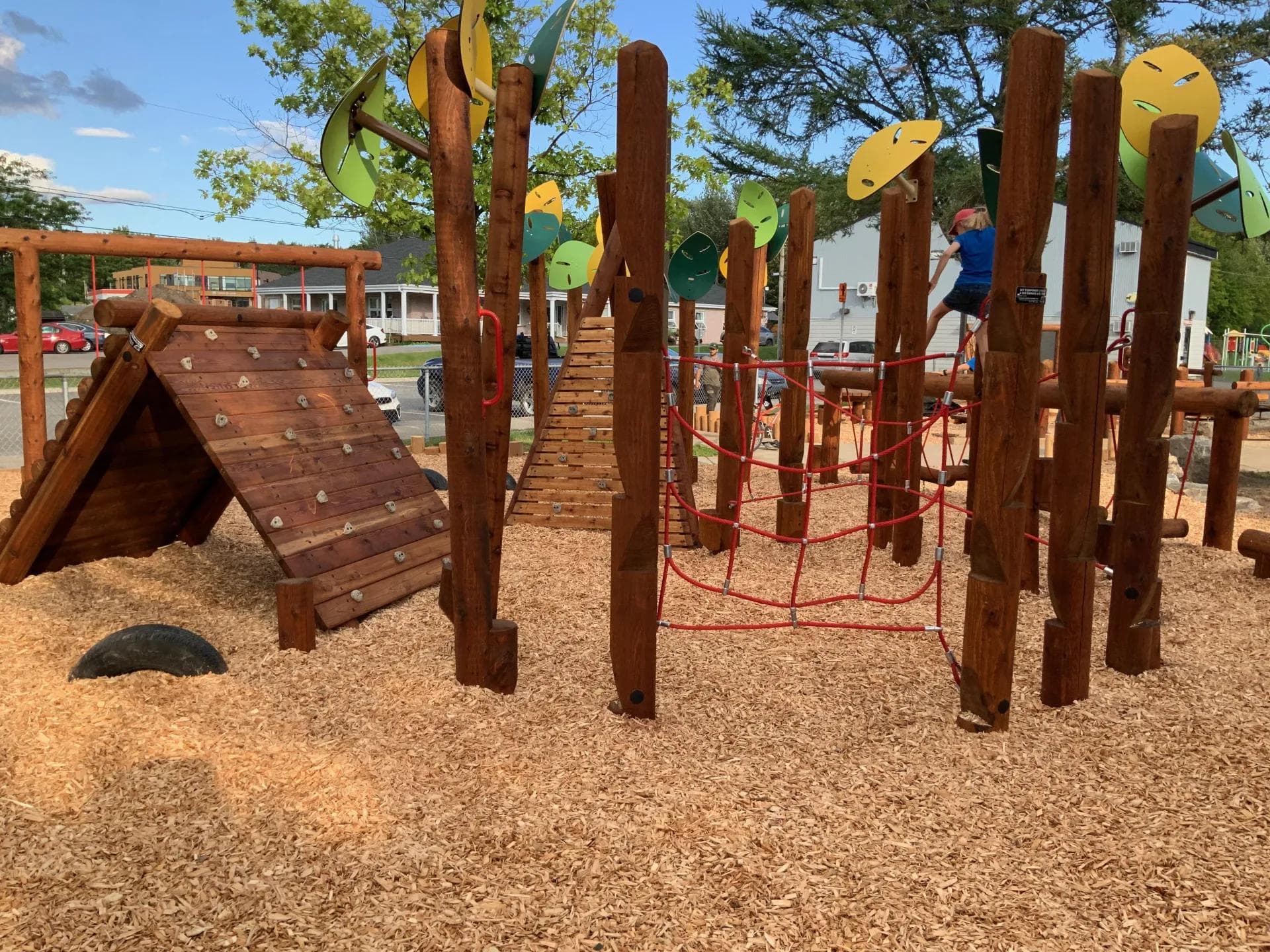 Child swinging from the overhead log ladder of a Westplay natural wood playground over wood fiber surfacing